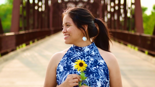 woman in blue and white floral sleeveless dress holding purple flower